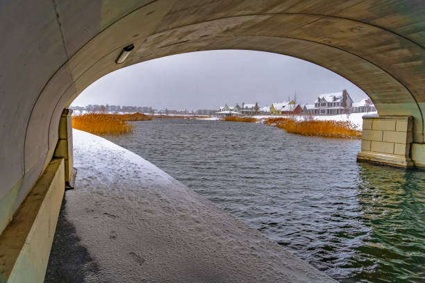 Snowy trail under a bridge at Oquirrh Lake in Utah. Snowy trail under the arched bridge at Oquirrh Lake viewed in winter. Homes amid a snow covered landscape can be seen in the distance.