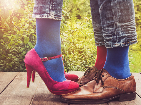 Men's and women's legs in fashionable shoes, bright, multi-colored socks on a wooden terrace on the background of green trees and sunny rays. Close-up. Concept of Style, Fashion and Beauty
