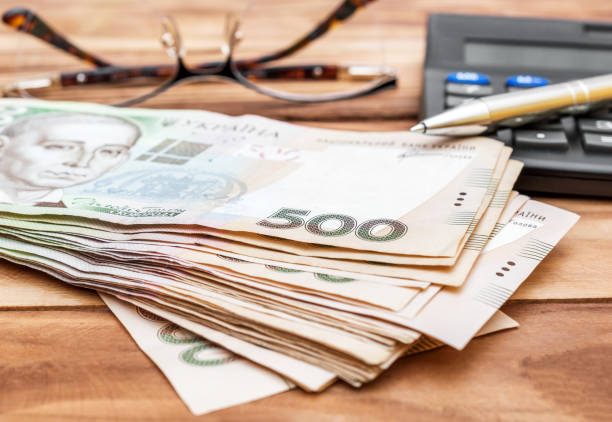 Heap of hryvnia bills with calculator and eyeglasses on wooden table. Close up. Heap of hryvnia bills with calculator and eyeglasses on wooden table. Close up. ukrainian currency stock pictures, royalty-free photos & images