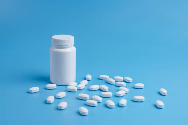istock White pills, tablets and white bottle on blue background. Copy space for text 1150565528