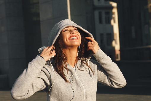 Young woman in gray hoodie enjoys music via headphones on the street