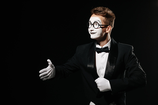 portrait of mime man in tuxedo and glasses giving hand for handshake on black background