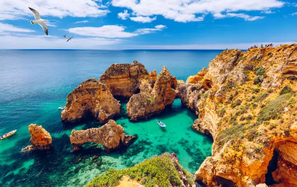 Photo of Panoramic view, Ponta da Piedade with seagulls flying over rocks near Lagos in Algarve, Portugal. Cliff rocks, seagulls and tourist boat on sea at Ponta da Piedade, Algarve region, Portugal.
