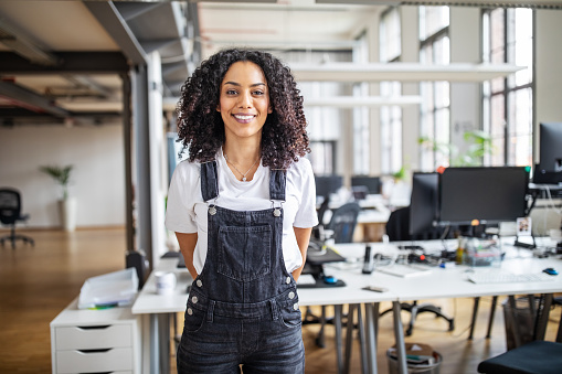 Portrait of mature african american businesswoman in casuals standing at her desk. Female professional looking at camera and smiling.