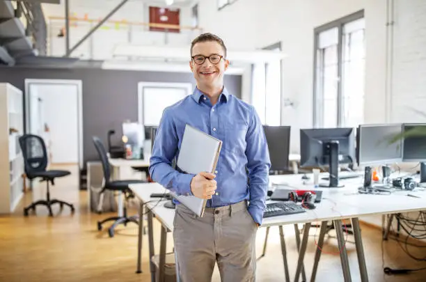 Portrait of confident mature businessman standing in office with a laptop. Smiling male professional in his office.