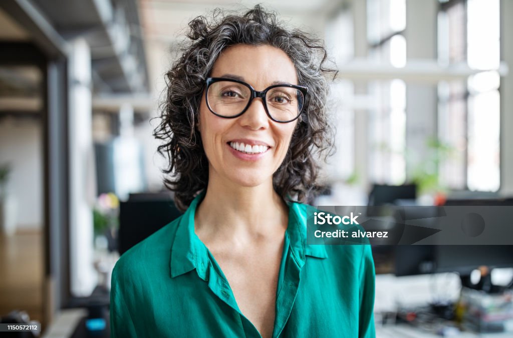 Close-up of a smiling mid adult businesswoman Close-up portrait of smiling mid adult businesswoman standing in office. Woman entrepreneur looking at camera and smiling Women Stock Photo