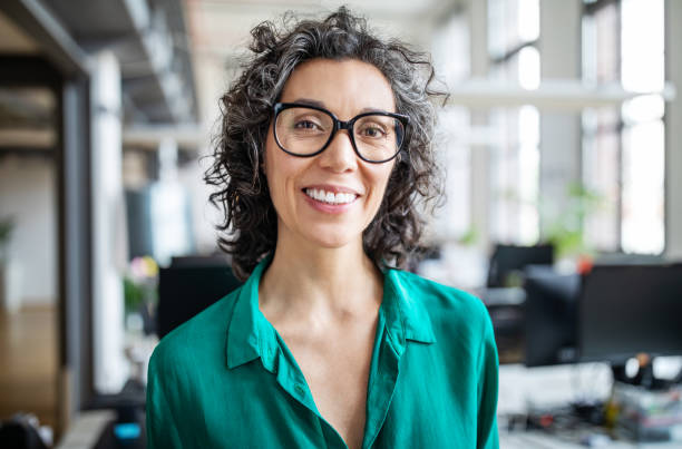 Close-up of a smiling mid adult businesswoman Close-up portrait of smiling mid adult businesswoman standing in office. Woman entrepreneur looking at camera and smiling professional portrait stock pictures, royalty-free photos & images