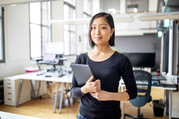 Businesswoman in smart casuals standing in office Portrait of confident young female professional at office with digital tablet. Businesswoman in smart casuals standing in office. woman waist up stock pictures, royalty-free photos & images