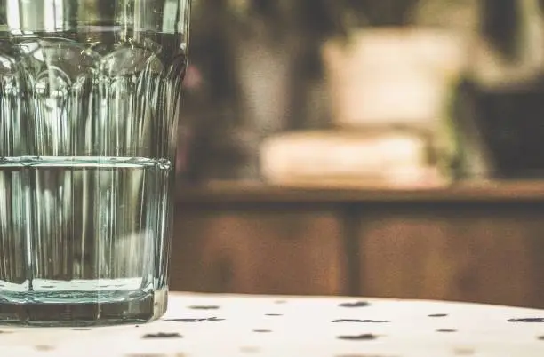 A tumbler of water, half full or half empty, resting on a kitchen table's floral table cloth.  Selective focus.