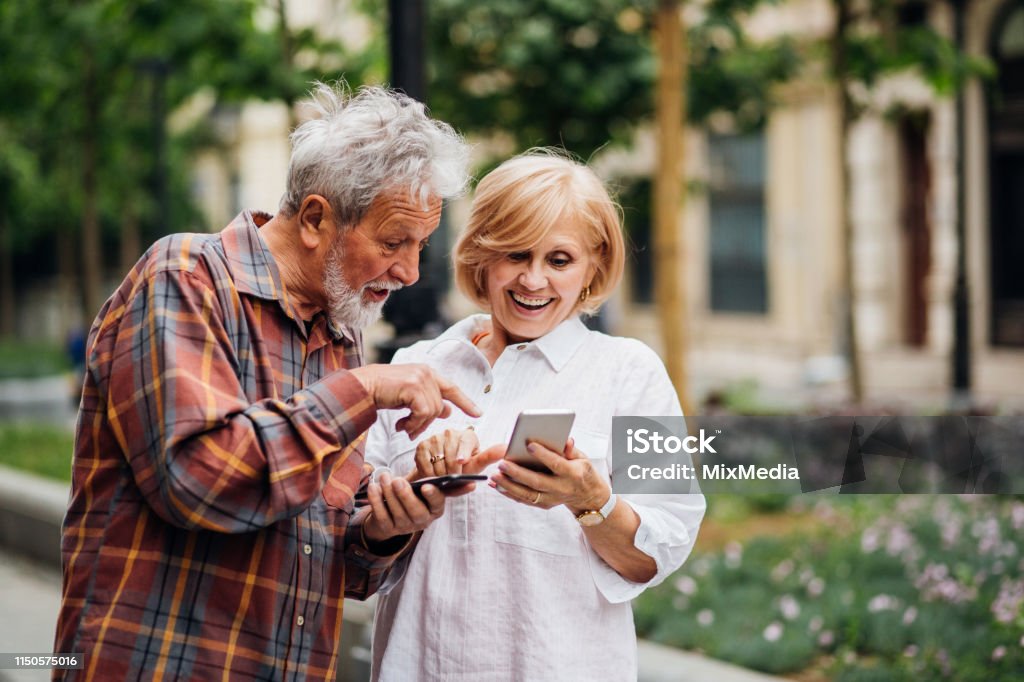 Charge Sharing Senior couple using smartphones Active Seniors Stock Photo