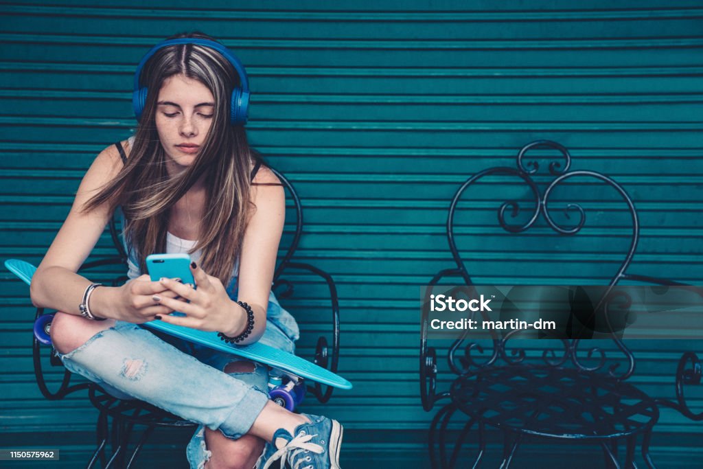 Teenage girl with skateboard texting Gen Z girl sitting against colorful wall and text messaging Generation Z Stock Photo