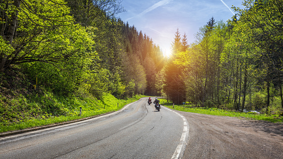 Bikers on mountainous highway, biker on the road in sunset light riding on curve road pass across Alpine mountains, extreme lifestyle, freedom concept. Austria, Alps