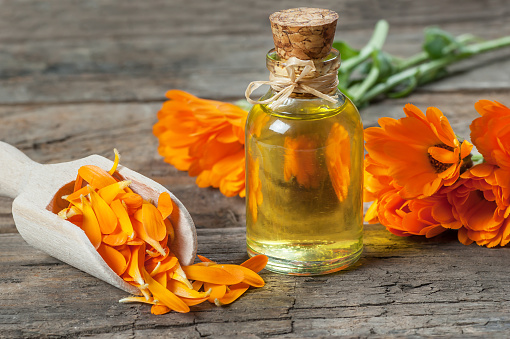 Glass bottle of calendula essential oil with fresh marigold flowers on wooden table