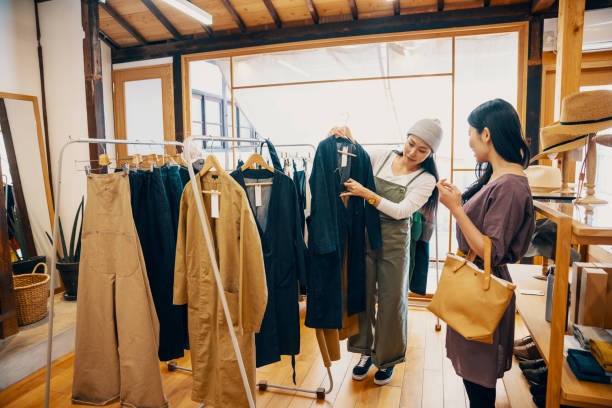 Retail shop clerk helping a mid adult woman customer shop for clothing in a boutique Retail shop clerk helping a mid adult woman customer shop for clothing in a boutique in Japan fashionable shopping stock pictures, royalty-free photos & images