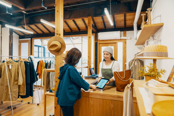 Female small business owner accepting mobile payment via digital tablet in a clothing store Female small business owner accepting mobile payment via digital tablet in a clothing store in Japan clothing store credit card stock pictures, royalty-free photos & images