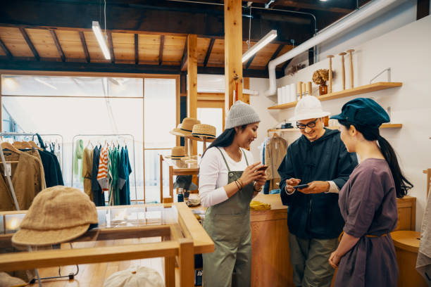 tres ancianos milleniales mirando sus teléfonos inteligentes en una tienda de ropa - small business saturday fotografías e imágenes de stock