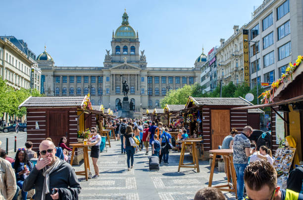 Easter food kiosks on Wenceslas Square with people in Prague during day of springtime. National museum of Prague and statue of St. Wenceslas behind