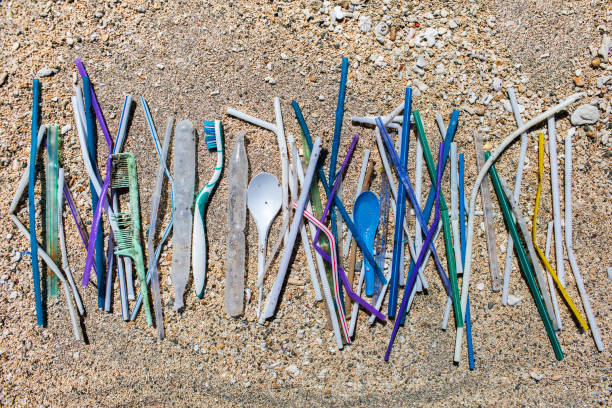 Heap of different plastic waste: straws and single-use spoons, toothbrush and comb collected on the beach on sand background