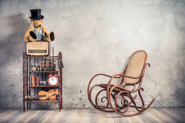 teddy bear in cylinder hat on vintage radio, antique books, clock, camera, binoculars, fiddle, keys on shelf, aged rocking chair front concrete wall background. retro old style filtered photo - radio 1930s imagens e fotografias de stock