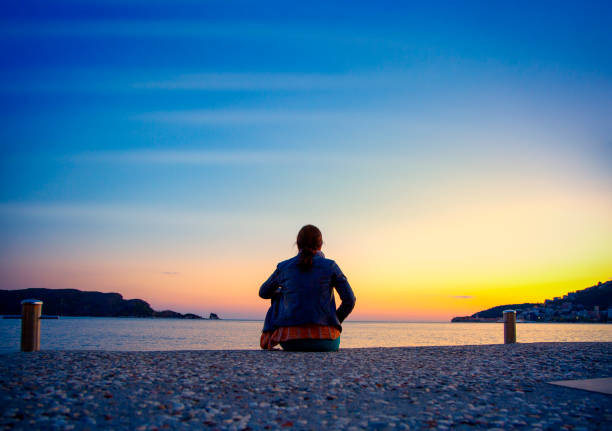Back shot of woman sitting on the dock enjoying the sunset. Perfect way to finish the day.