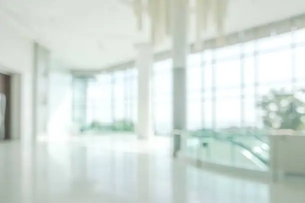 Photo of Hotel or office lobby blur background interior view toward reception hall, modern luxury white room space with blurry corridor and building glass wall window