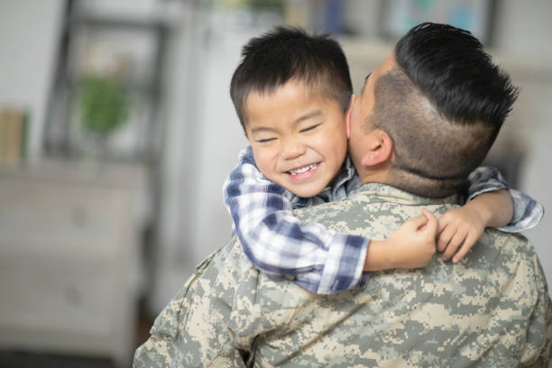 Giving dad a big hug A military dad and his son are hugging in their living room. The son is so excited that he is home that he is squeezing him as hard as he can. filipino family reunion stock pictures, royalty-free photos & images