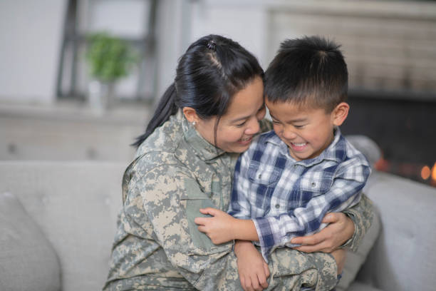 Military Mom Hugging Her Son A mother and her son are hugging in their living room. The mother is wearing a military uniform while the boy has a giant smile on his face. He is so excited that she is home. filipino family reunion stock pictures, royalty-free photos & images