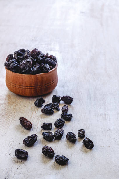 Dark blue raisins in a wooden bowl on a bright white background. Close-up. Insulated. stock photo