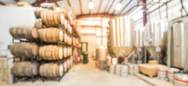 Panoramic view blurry background stack of barrels in cellar at American brewery Panorama blurred image modern beer plant (brewery), stainless steel brewing equipments and stack of barrels in cellar. Row large tanks in microbrewery. Brewery production vats, fermentation interior microbrewery stock pictures, royalty-free photos & images