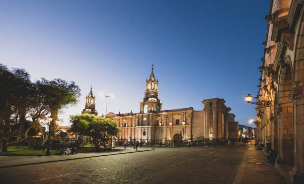 People walking next to the Basilica Cathedral of Arequipa at Plaza de Armas, Peru, at night.