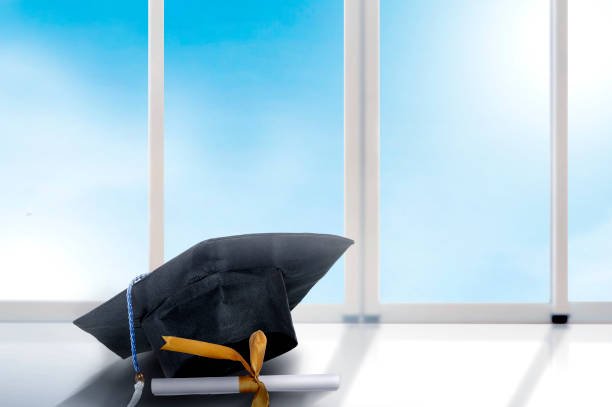 istock Mortarboard hat and diploma on the table with window glass and blue sky background 1150637457