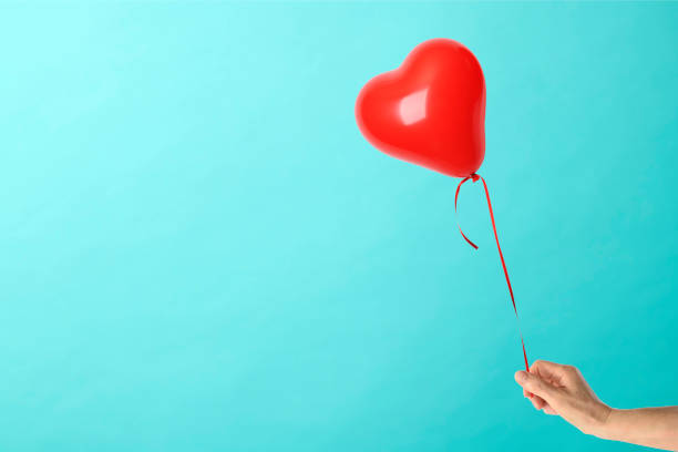 istock Holding a red heart shape balloon against blue background 1150644386