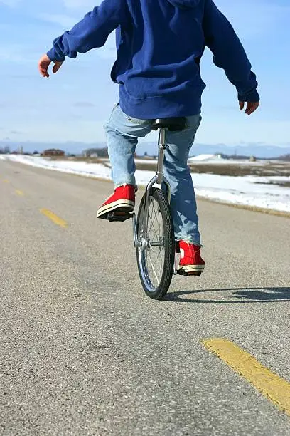 youth riding unicycle on road in red shoes