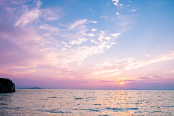 Sun setting in the distance over the seascape, coloring clouds pink and purple