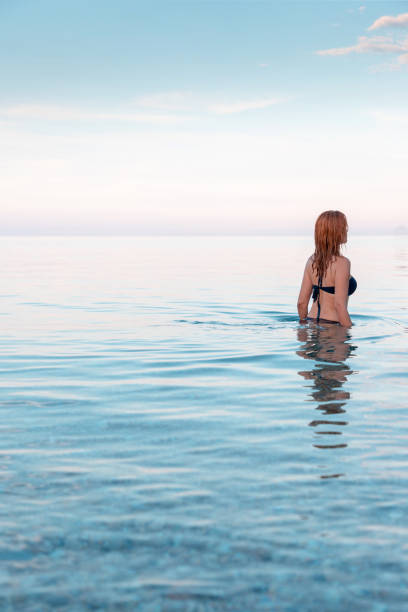 istock Pretty redhead woman getting into calm sea 1150653951