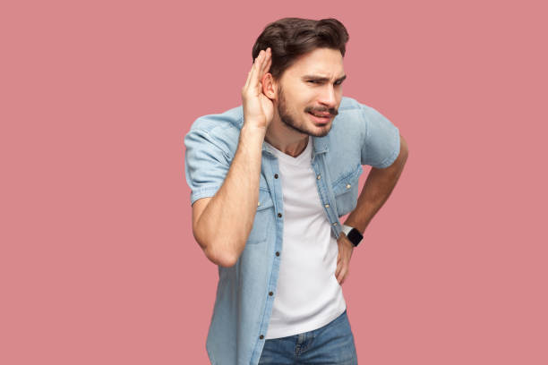 retrato do homem novo barbudo considerável atento na camisa ocasional azul do estilo que está com mão na orelha e que tenta ouvir algo com face séria. - spy secrecy top secret mystery - fotografias e filmes do acervo