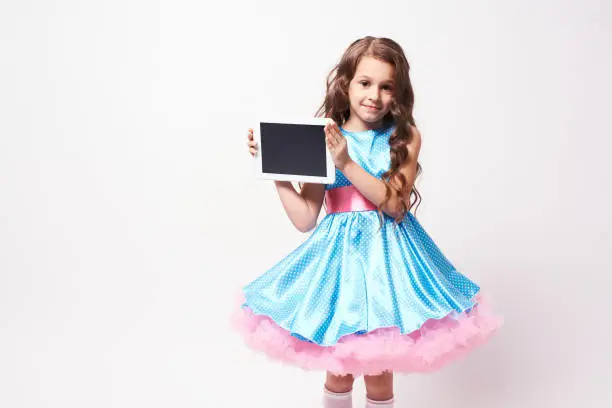Little girl. Modern tablet. Fluffy dress.