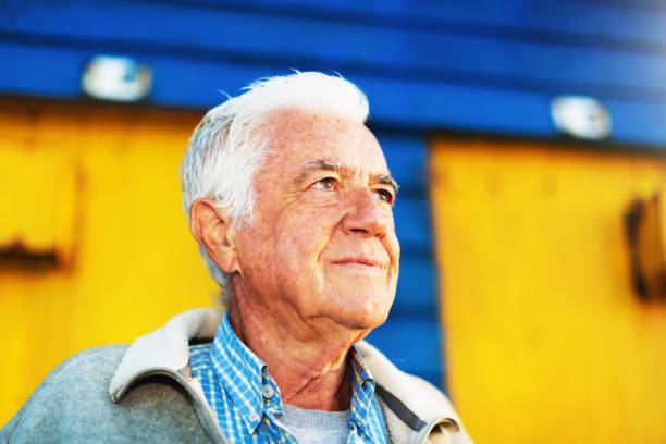 istock Senior man smiling by brightly painted beach hut 1150680943