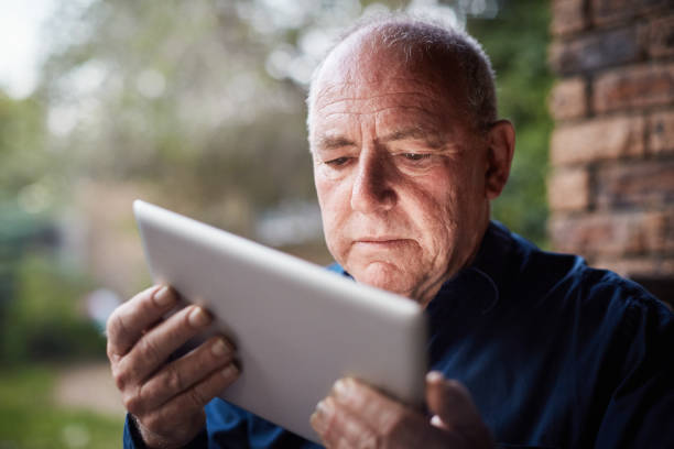 el hombre mayor que usa la tableta digital parece confundido, frunciendo el ceño - entrecerrar los ojos fotografías e imágenes de stock
