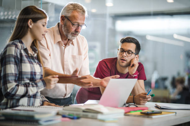 istock Mature teacher and his students talking while using laptop at campus. 1150686407
