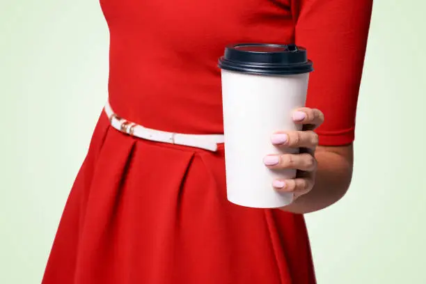 Girl hold white paper glass. Fragrant hot coffee to go away. Red dress background