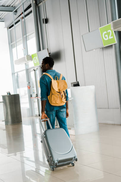 istock back view of african american man in denim outfit walking with suitcase and backpack in airport 1150686607