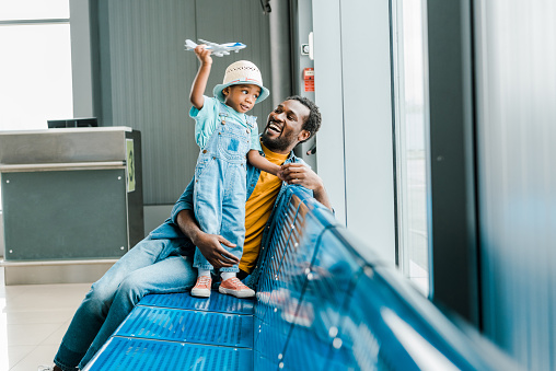 feliz padre afroamericano mirando a su hijo mientras niño jugando con el avión de juguete en el aeropuerto photo