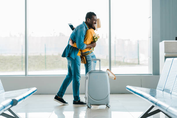 happy african american man with bouquet of tulips hugging girlfriend with suitcase and passport in airport happy african american man with bouquet of tulips hugging girlfriend with suitcase and passport in airport airport hug stock pictures, royalty-free photos & images