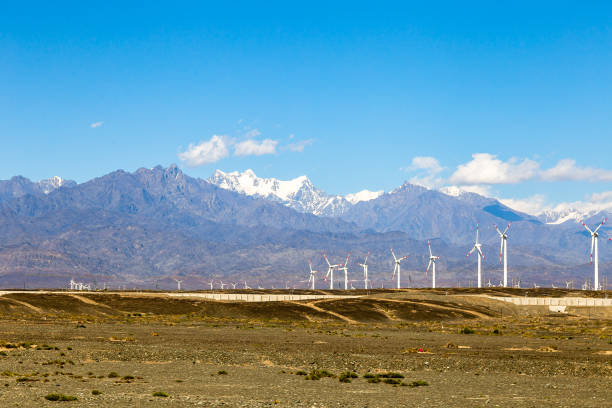 aug 2017 – xinjiang, china – een windmolenpark in de buurt van urumqi, met de majestueuze hoogte van tianshan erachter. de woestijnen van xinjiang, de meest westelijke provincie van china, zijn volledig van de machtsinstallaties van de wind turbine - urumqi stockfoto's en -beelden