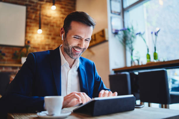 istock Businessman using tablet in cafe and having phone call on wireless headphones 1150690596