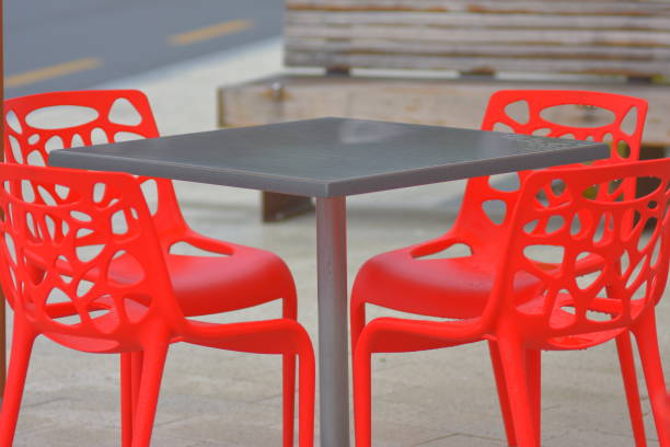 Red plastic outdoor chairs placed around gray square table with single central post.