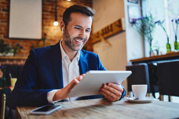 homme utilisant la tablette et le casque sans fil tout en ayant le café dans le café - hot drink audio photos et images de collection