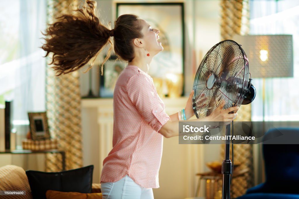 femme au foyer souriant appréciant l’air frais devant le ventilateur de travail - Photo de Chaleur libre de droits