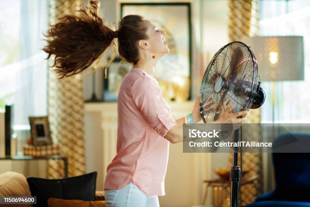 Photo libre de droit de Femme Au Foyer Souriant Appréciant Lair Frais Devant Le Ventilateur De Travail banque d'images et plus d'images libres de droit de Chaleur